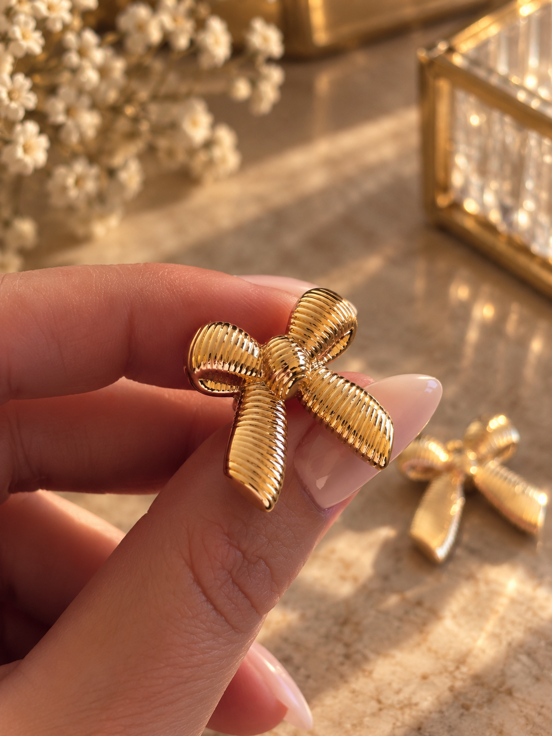 Apzeltīti bantīšu auskari rokā, elegants rotas dizains tuvplānā